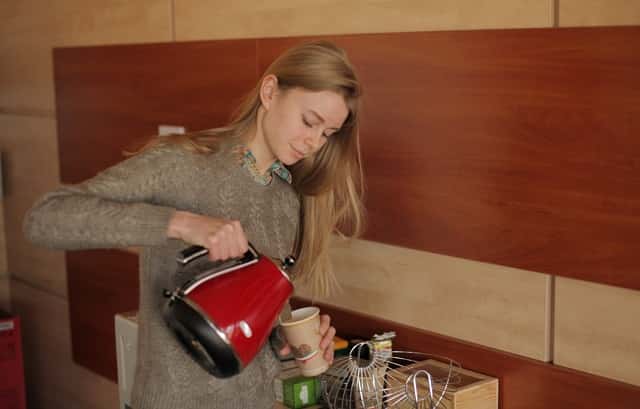 ポットからカップに飲み物を注ぐ女性
