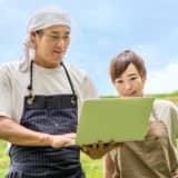 パソコンを見て畑にいる男女
