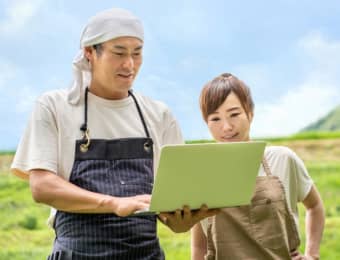 パソコンを見て畑にいる男女